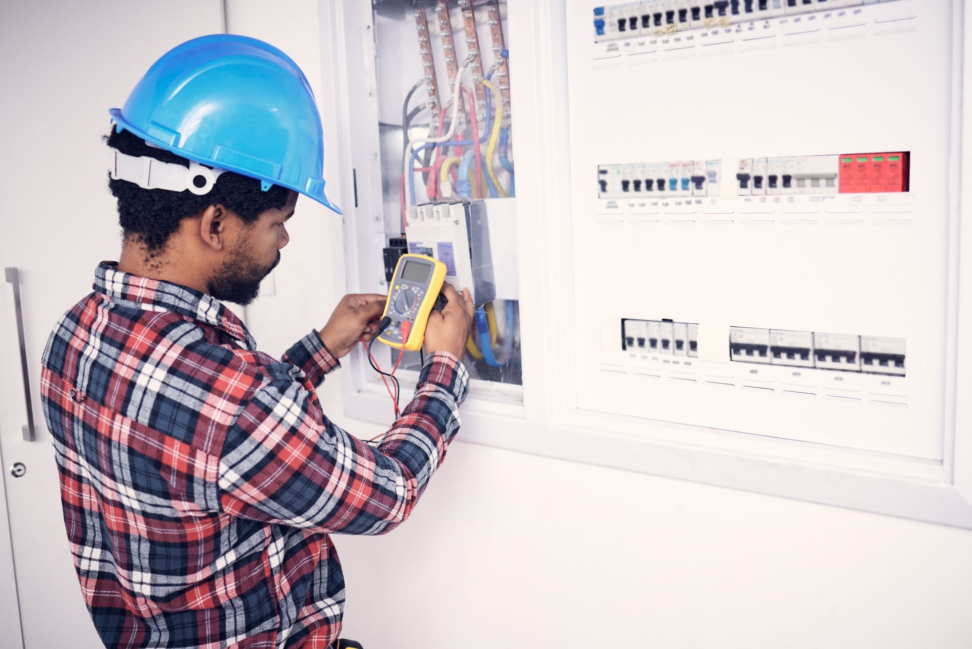 A man wearing a hard hat is working on an electrical box.