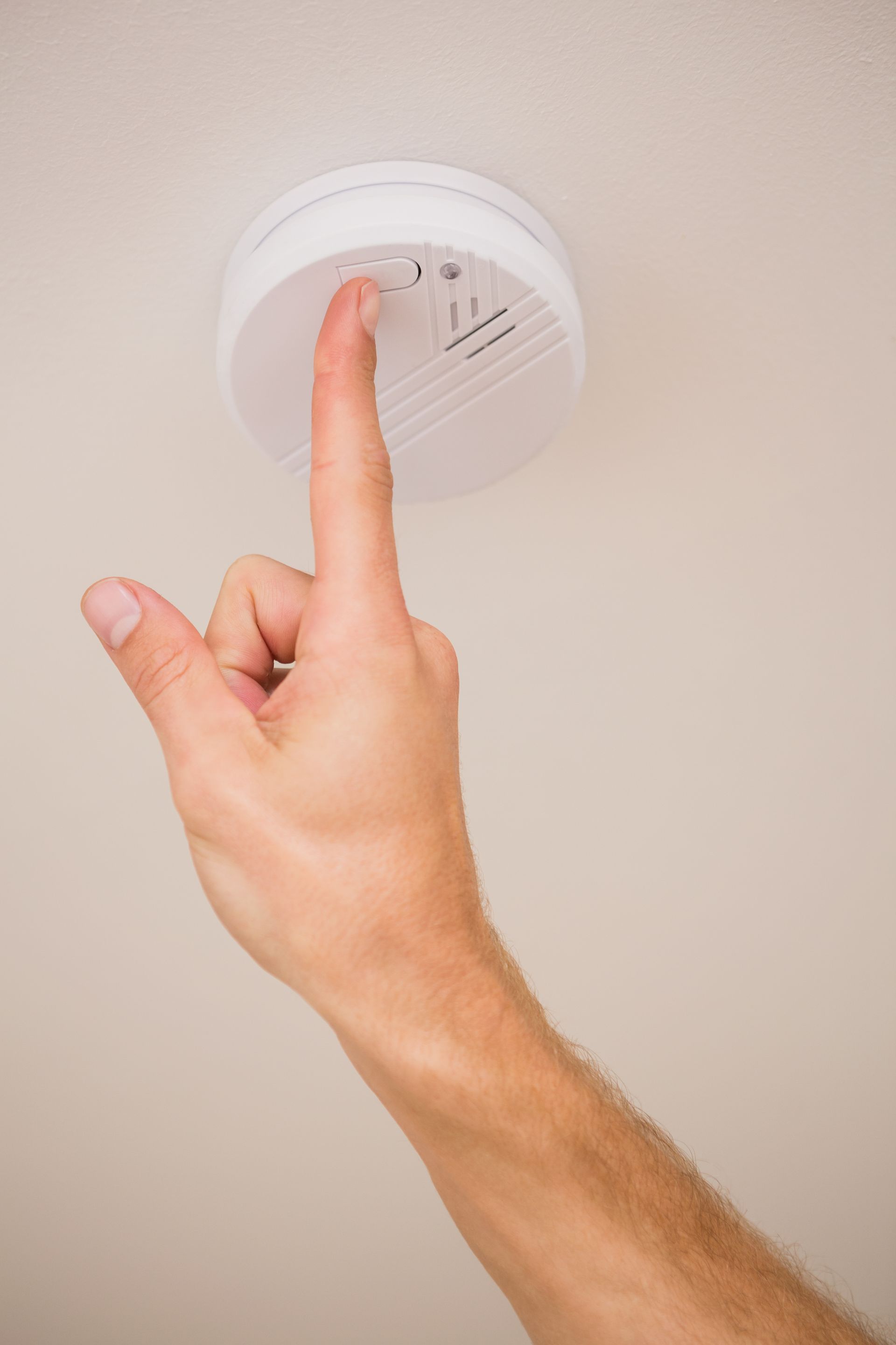 A person is pressing a button on a smoke detector.