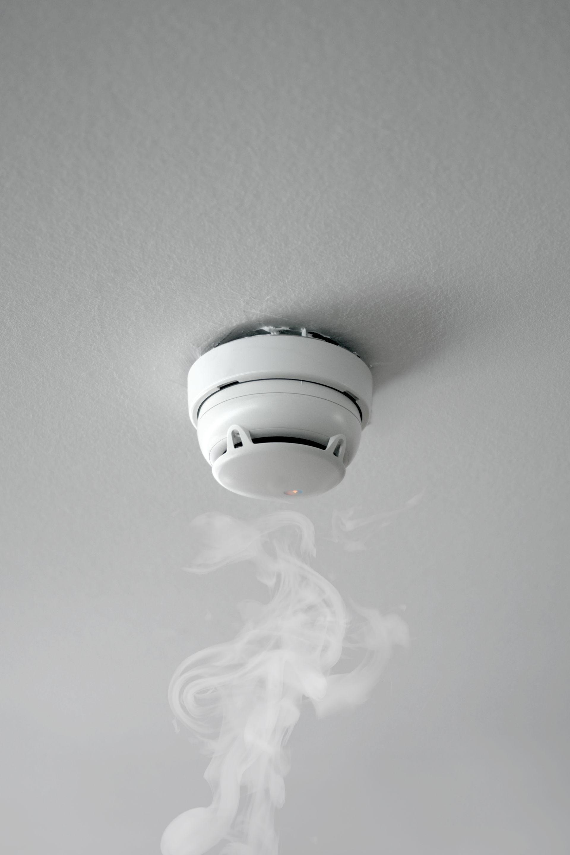 A smoke detector on the ceiling with smoke coming out of it.