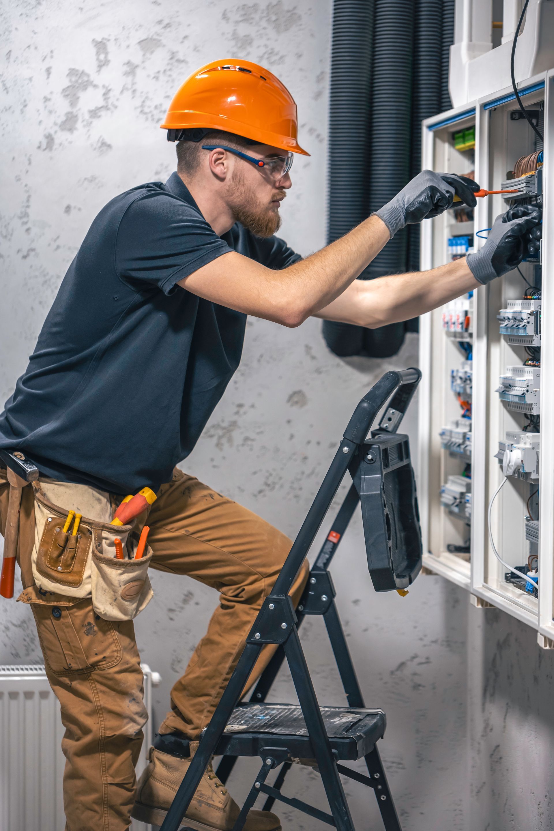 A man is standing on a ladder working on an electrical box.