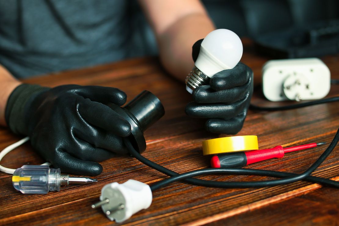 A person is holding a light bulb in their hands on a wooden table.