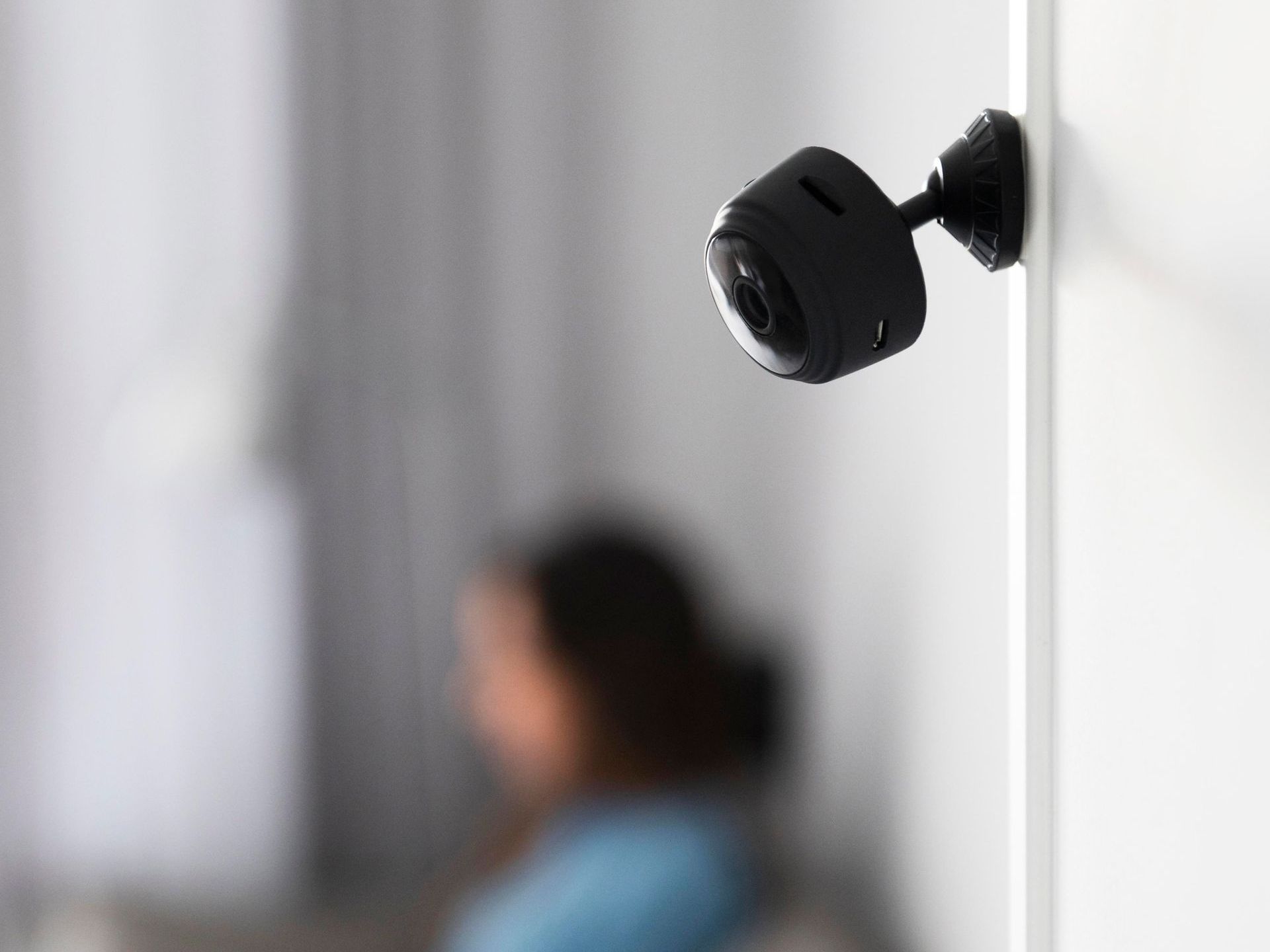 A person is sitting on a couch in a living room with a camera on the wall.