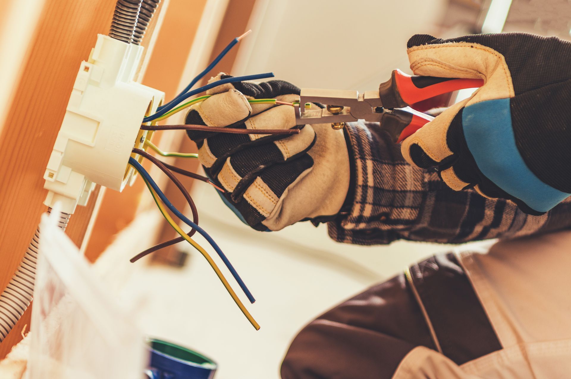 An electrician is working on an electrical outlet with a pair of pliers.