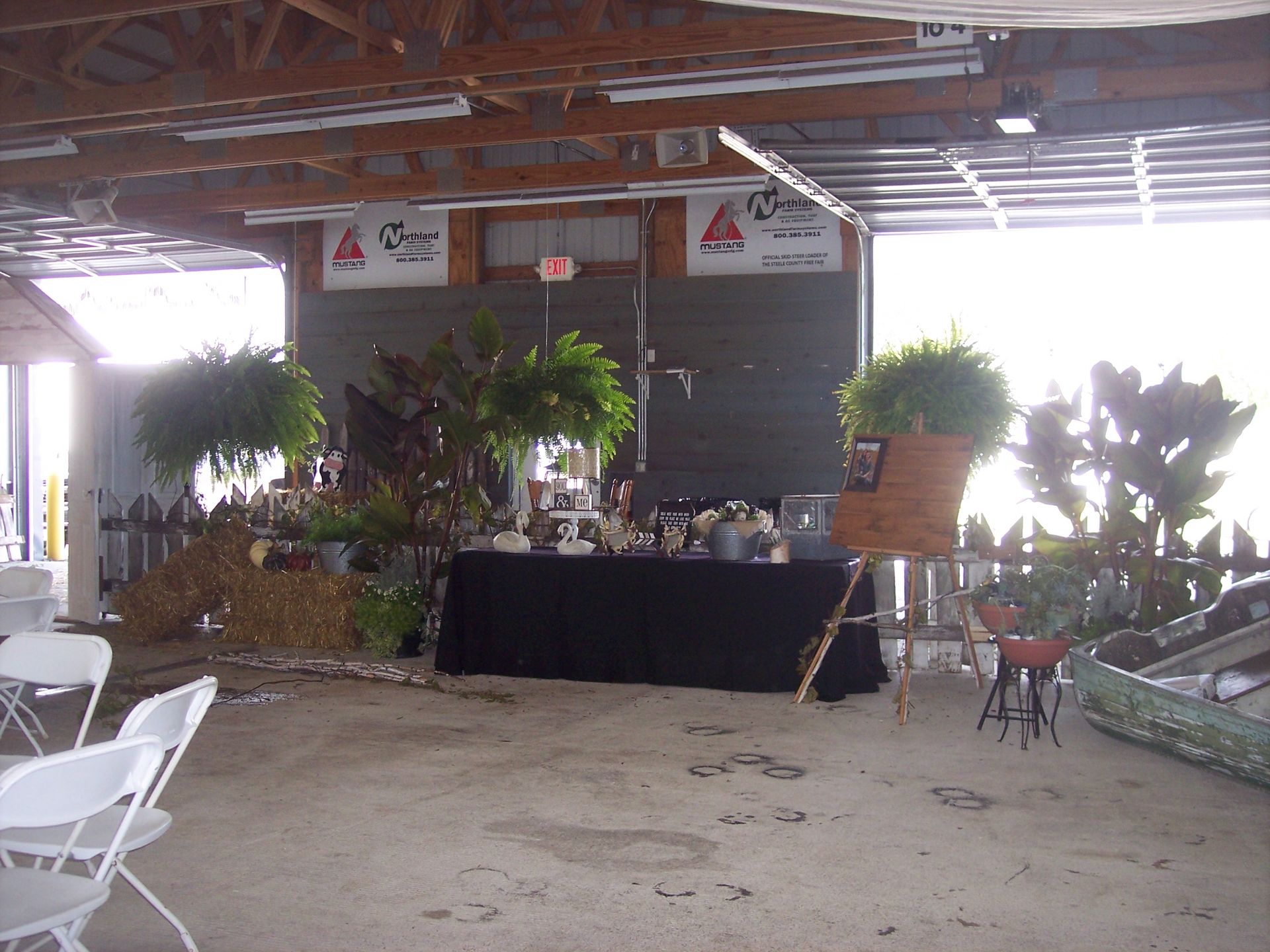 A decorated table set for an event inside a rustic, open-air building with white chairs in the foreground.