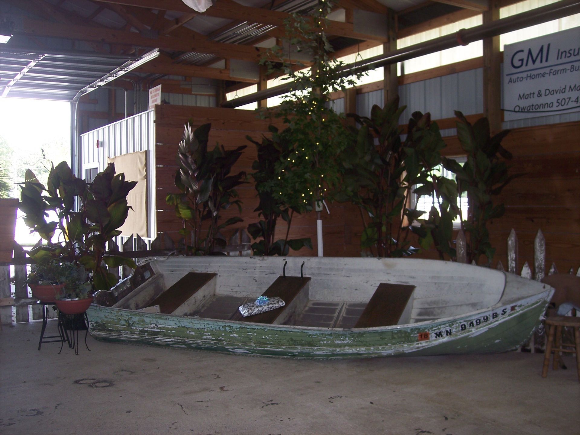 A vintage green and white rowboat displayed indoors as decor, surrounded by potted plants and a small lit tree.