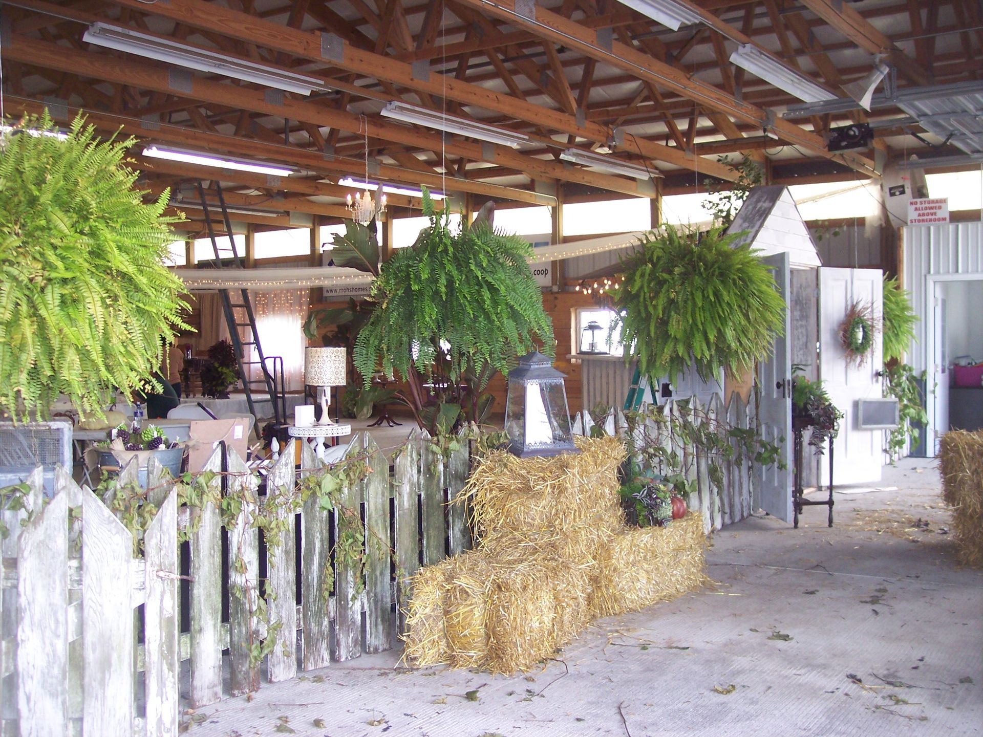 Hay bales, ferns, and a picket fence inside a rustic barn.