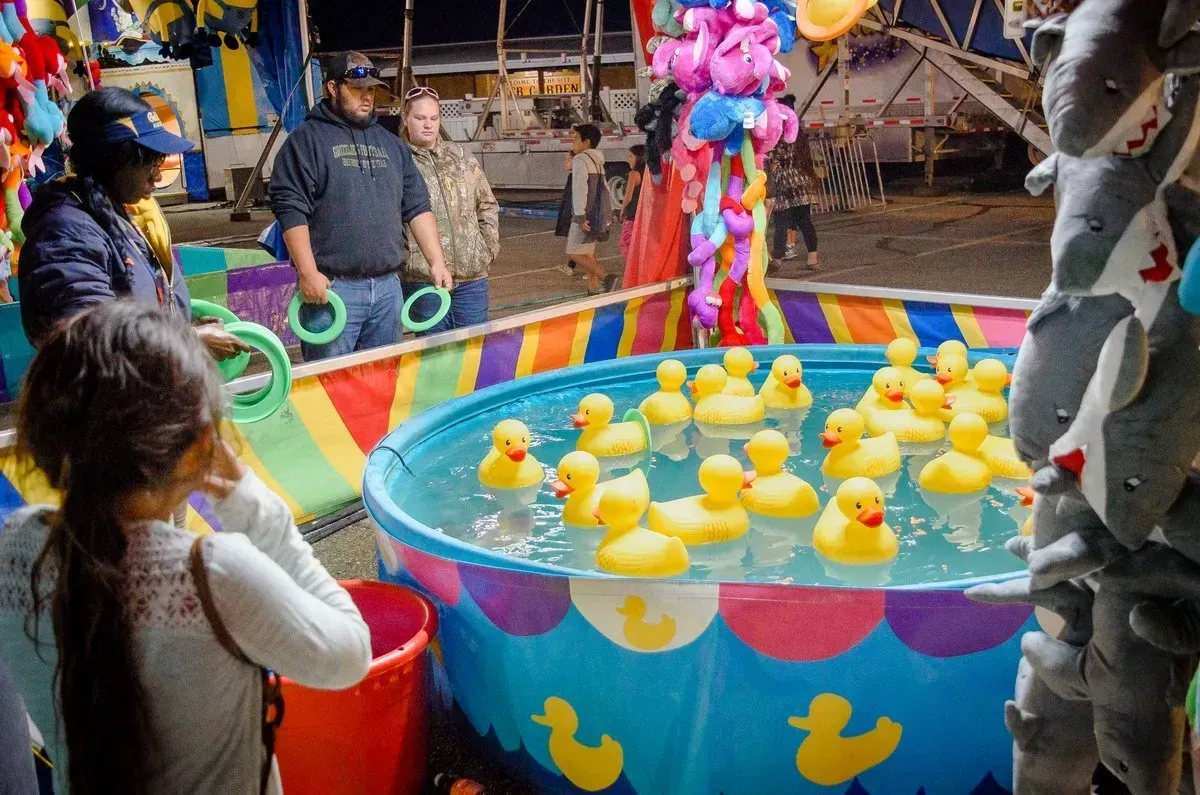 Child playing ring toss game at a carnival, trying to toss rings onto yellow rubber ducks in a pool.