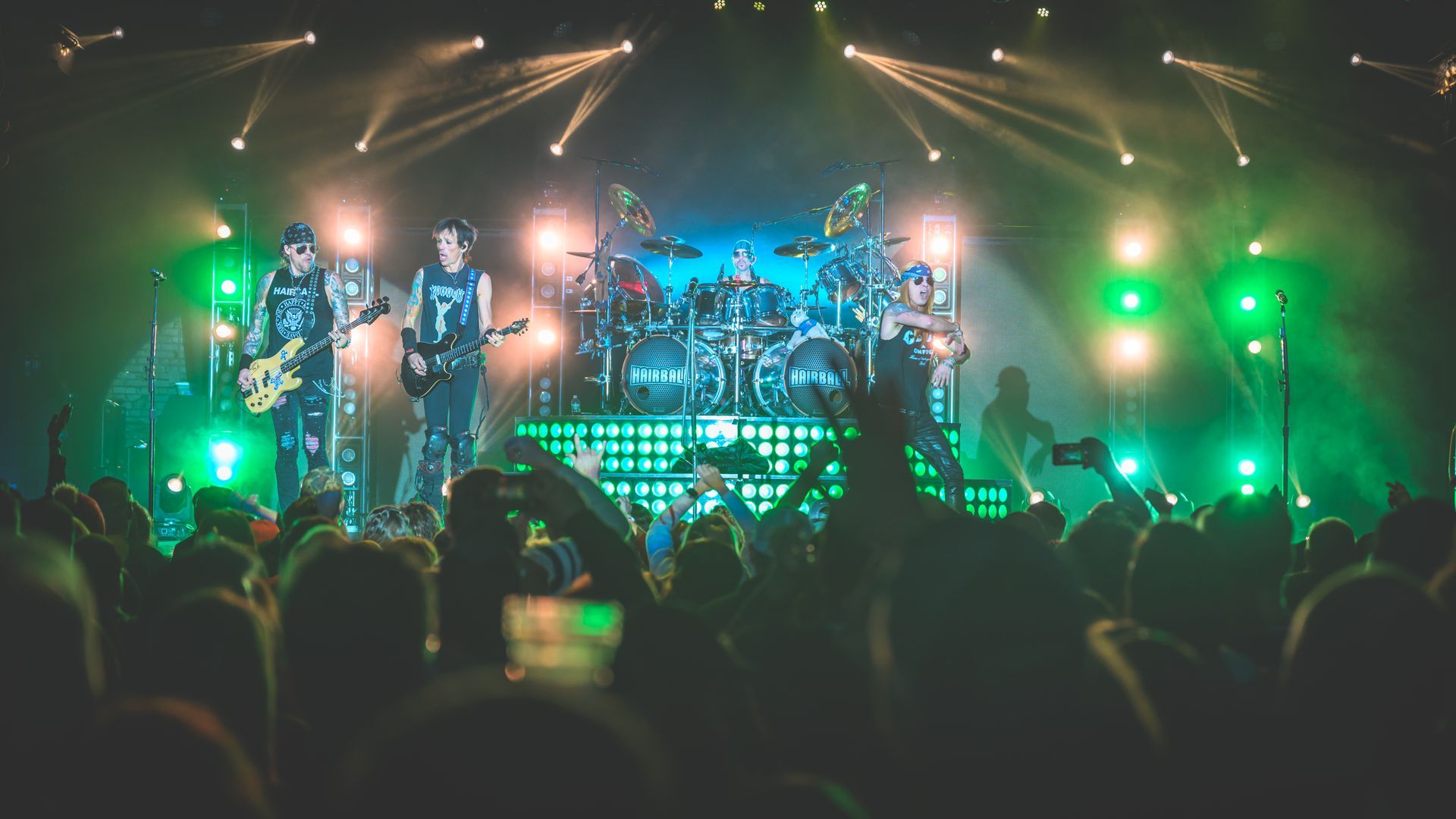 Hairball Band performing on stage, brightly lit with green lights; crowd cheering.
