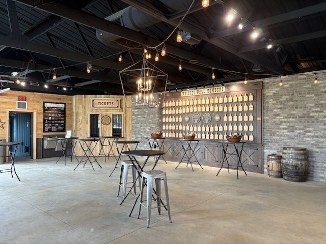 A rustic indoor event space with high black ceilings, stone walls, high-top tables, and a display of bottled spirits.