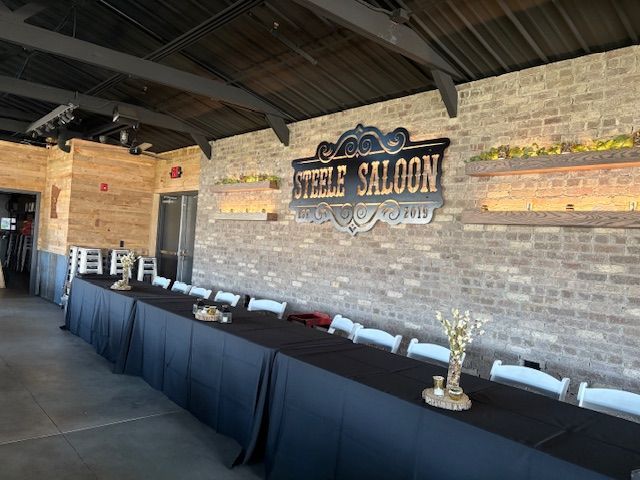 Steele Saloon sign on a brick wall, long tables set for an event, white chairs, black tablecloths.