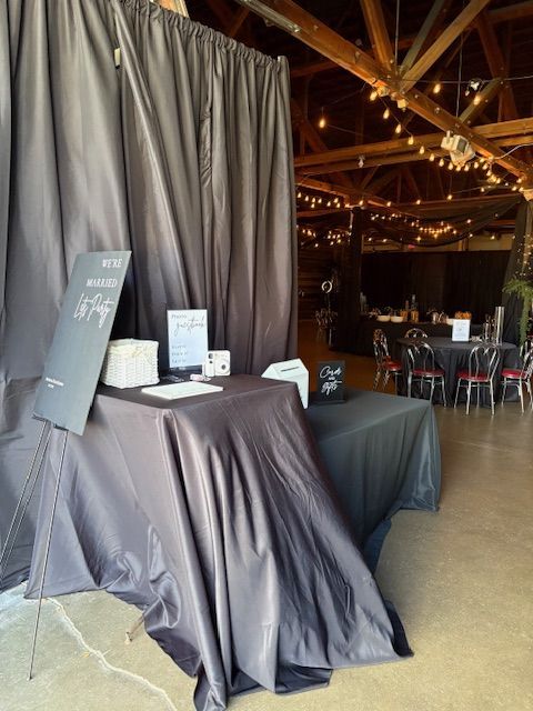 Entry table with draped black cloth, welcome sign, and event venue in the background.