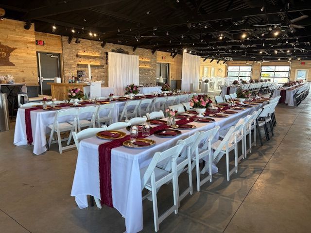 A banquet hall set for a wedding reception with long tables covered in white tablecloths and burgundy runners.