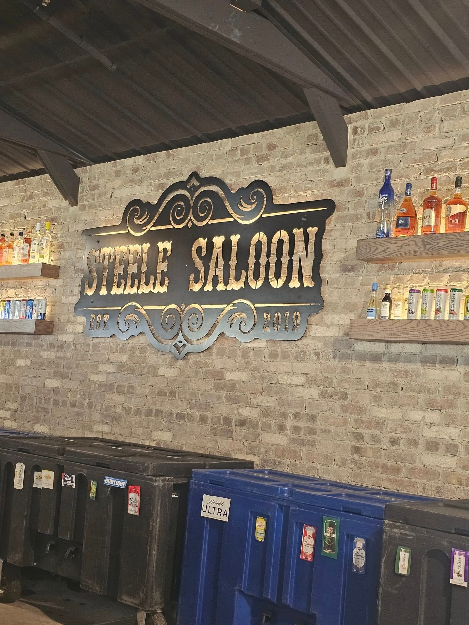 A rustic brick wall features a dark, ornate sign reading 