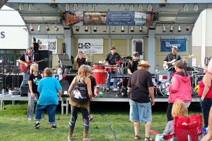 Band performing on a stage outdoors; crowd dancing on grass.