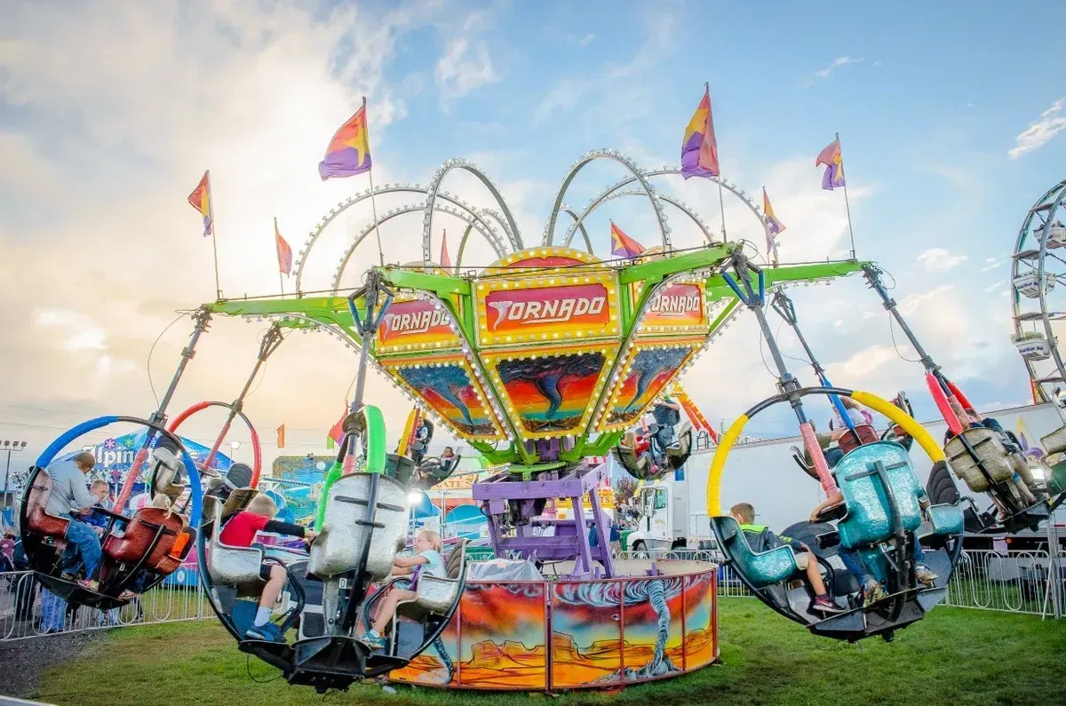 Tornado amusement park ride with people. Spinning ride with colorful lights and flags, blue sky.