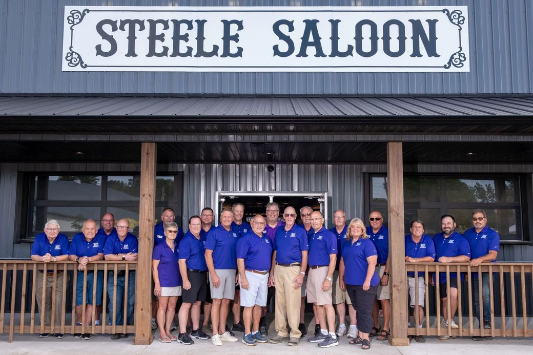 Group of people in blue shirts stand in front of the Steele Saloon.