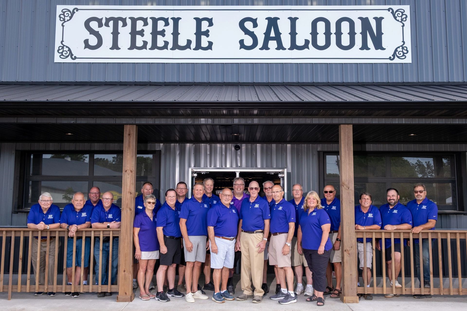 Group of people in blue shirts stand in front of the Steele Saloon.