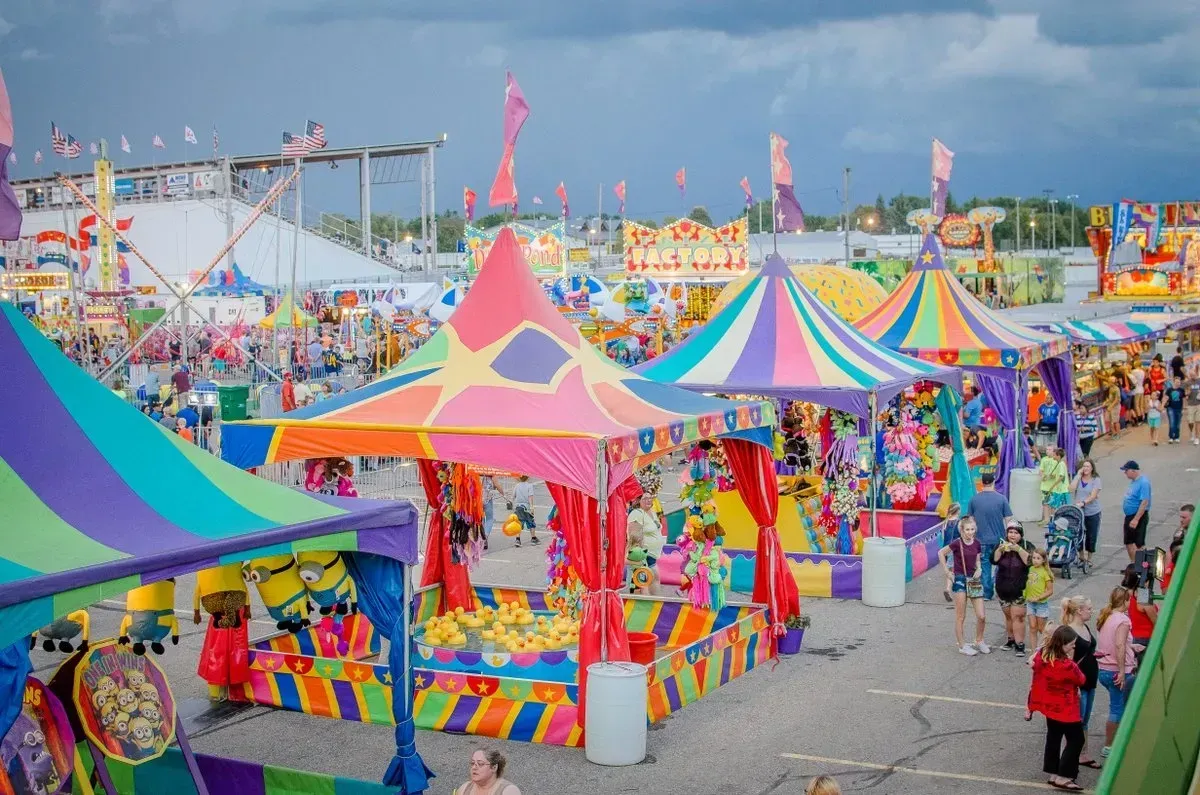 Carnival games and brightly colored tents at a fair, people playing games and walking around.