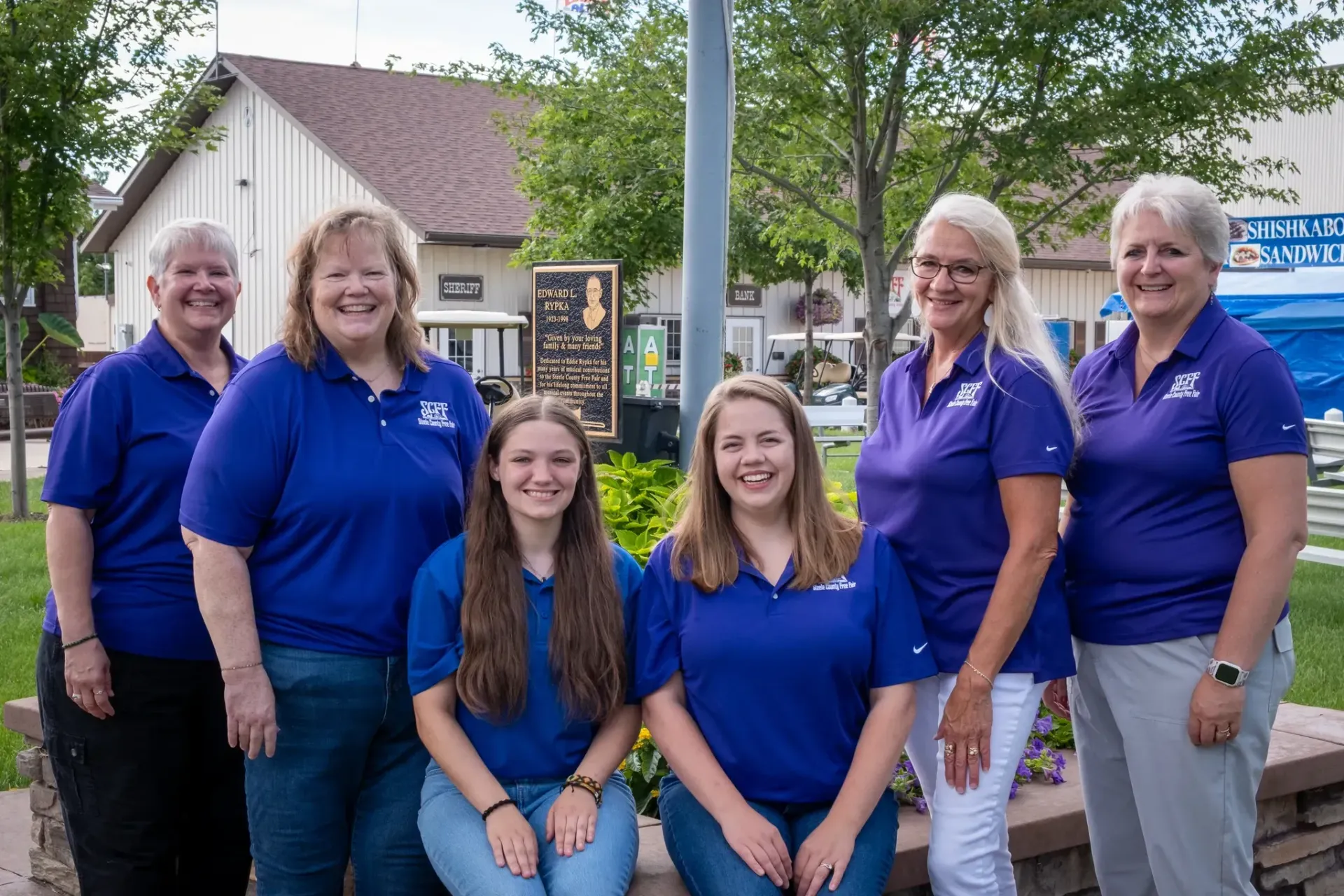Group of six people in blue shirts posing outdoors.