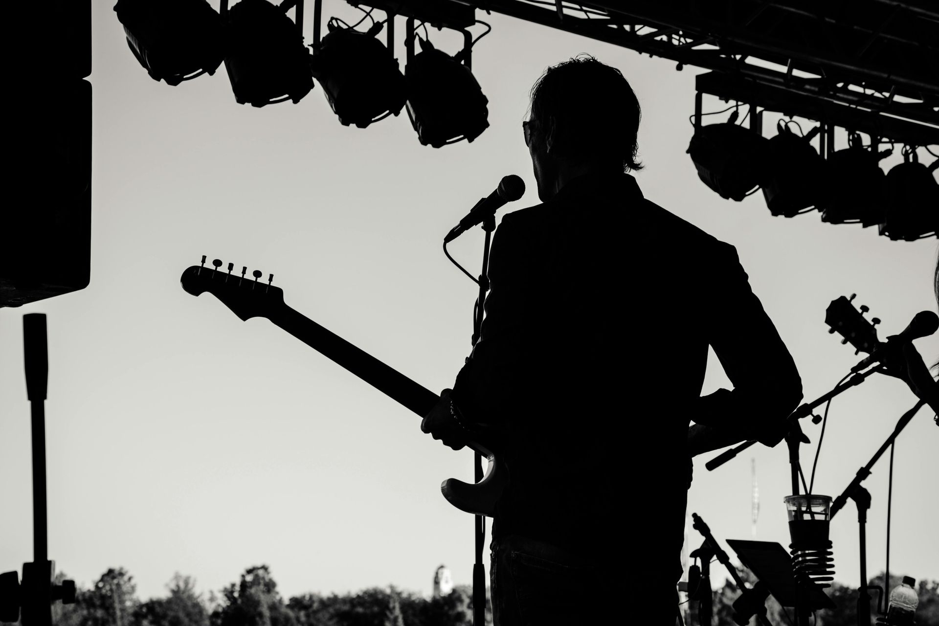 Silhouette of a guitarist on stage, holding a guitar, with microphones and stage lights.