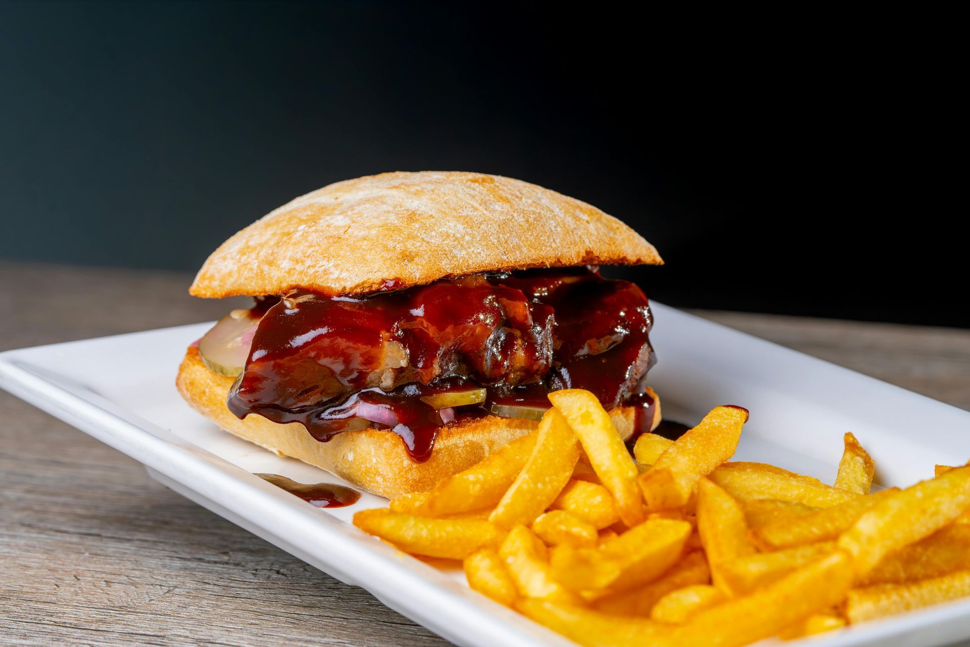 Glazed burger on a white plate with golden fries on a wooden table