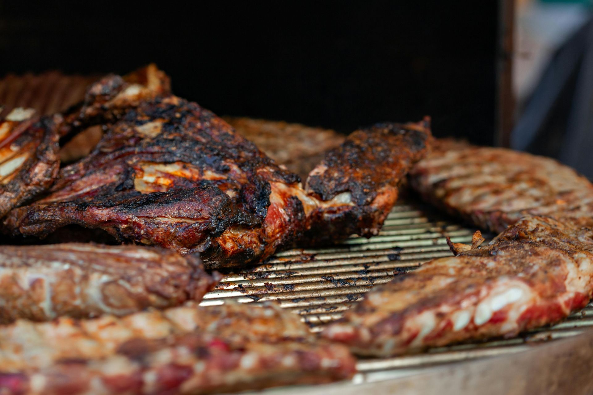 Grilled ribs and meat on a metal grill; charred exterior, close-up shot.