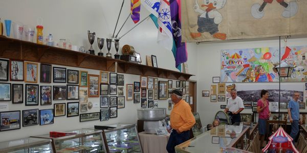 Interior of a museum with a display of photos, trophies, and people. A man in orange stands near a glass case.