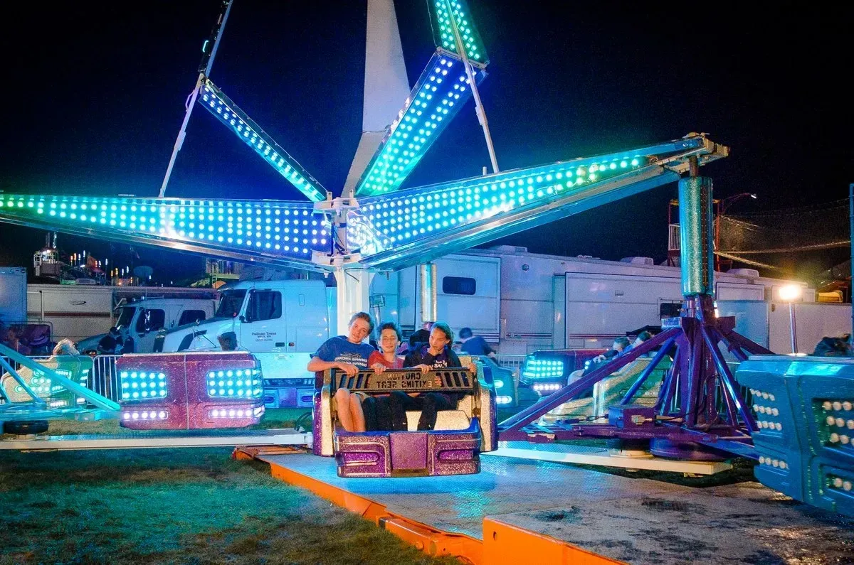 People on a carnival ride lit with blue and green lights at night.