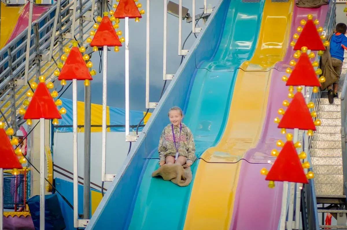 Child sliding down a colorful amusement park slide. Red triangles line the slide.