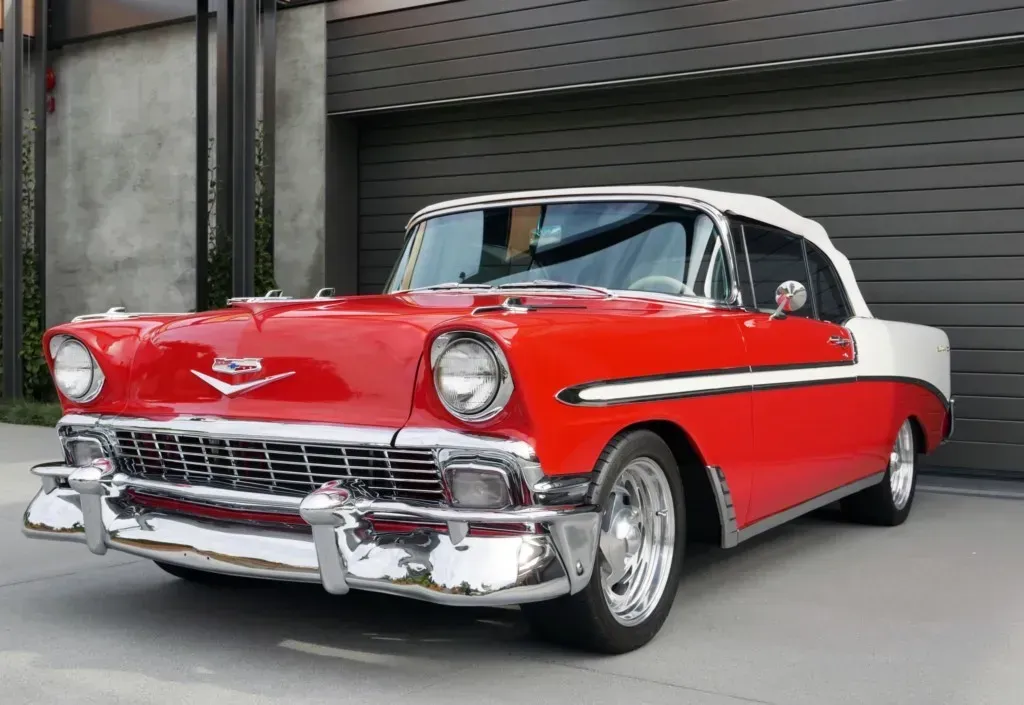 Red and white classic Chevrolet Bel Air convertible parked in front of a modern garage.