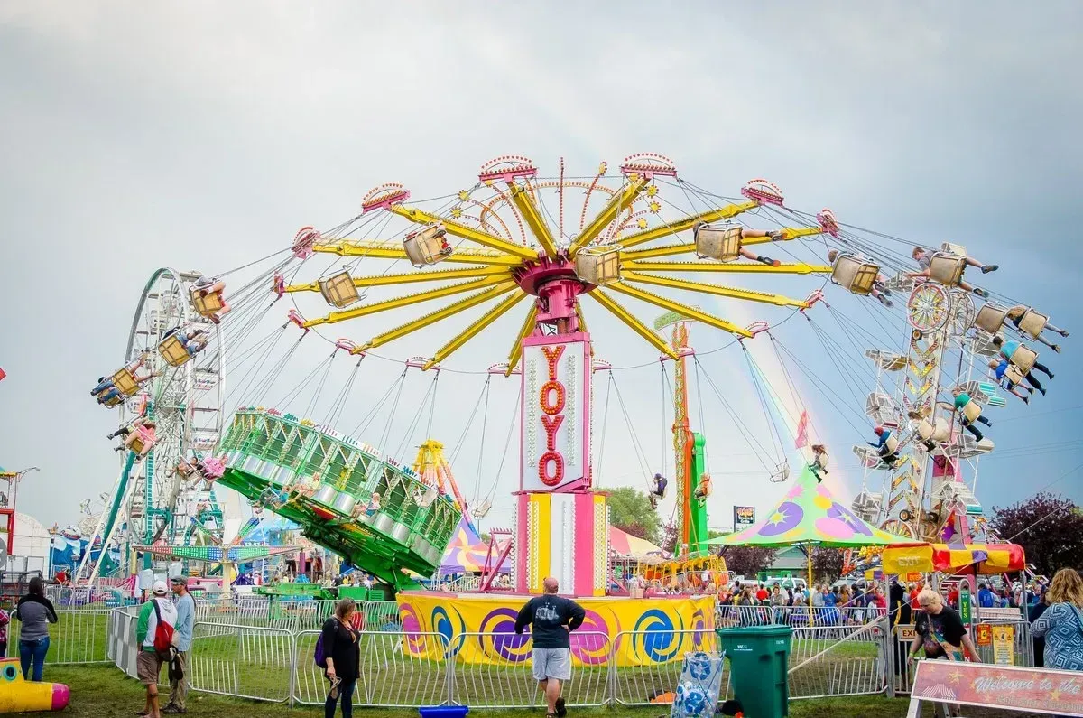 Carnival scene with a swing ride and Ferris wheel under a cloudy sky. People are visible.
