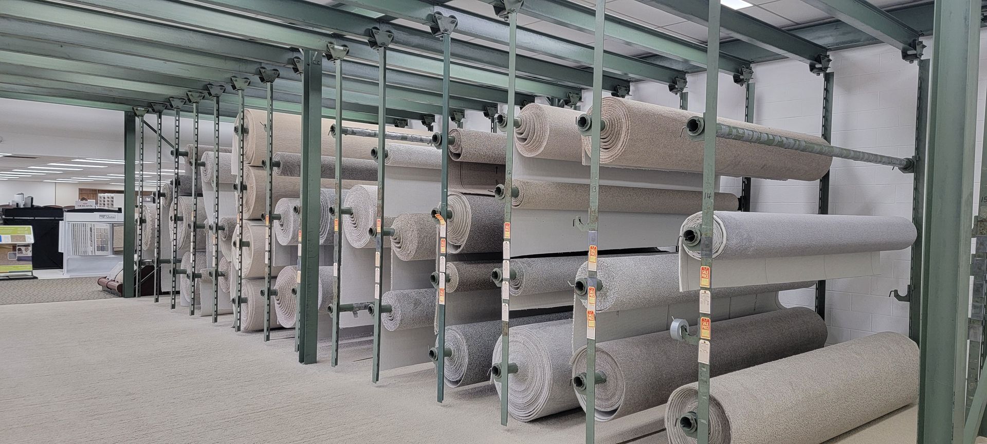 Rows of carpet rolls stored on metal racks in a warehouse.
