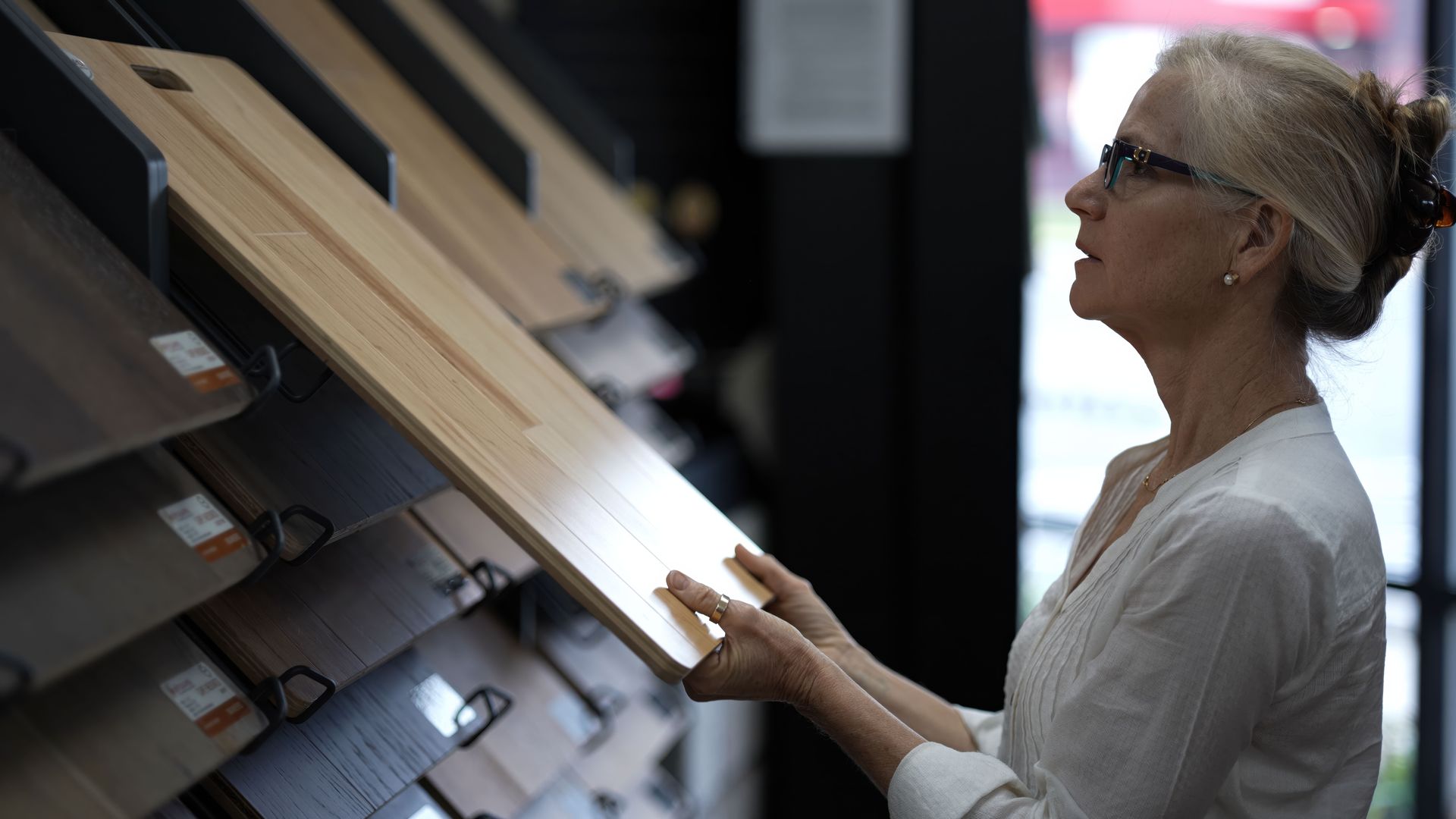 Wood veneer samples fanned out on a wood-grain surface, showcasing various shades and patterns. Woman examining wood flooring samples in a showroom, holding one up to compare.