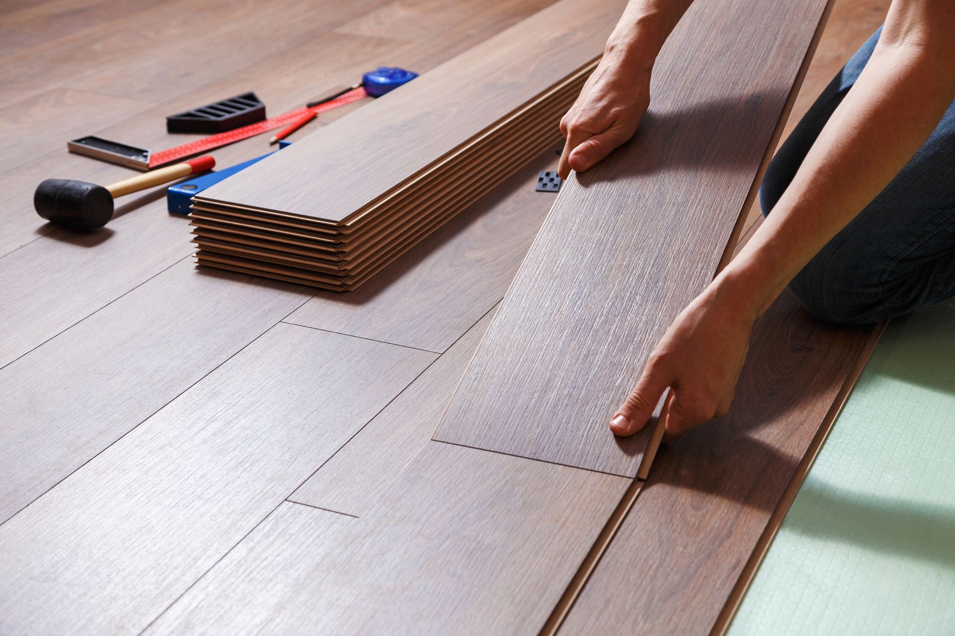 Person installing wood flooring, connecting planks. Tools and stacked planks in view. Person installing wood flooring, connecting planks. Tools and stacked planks in view.