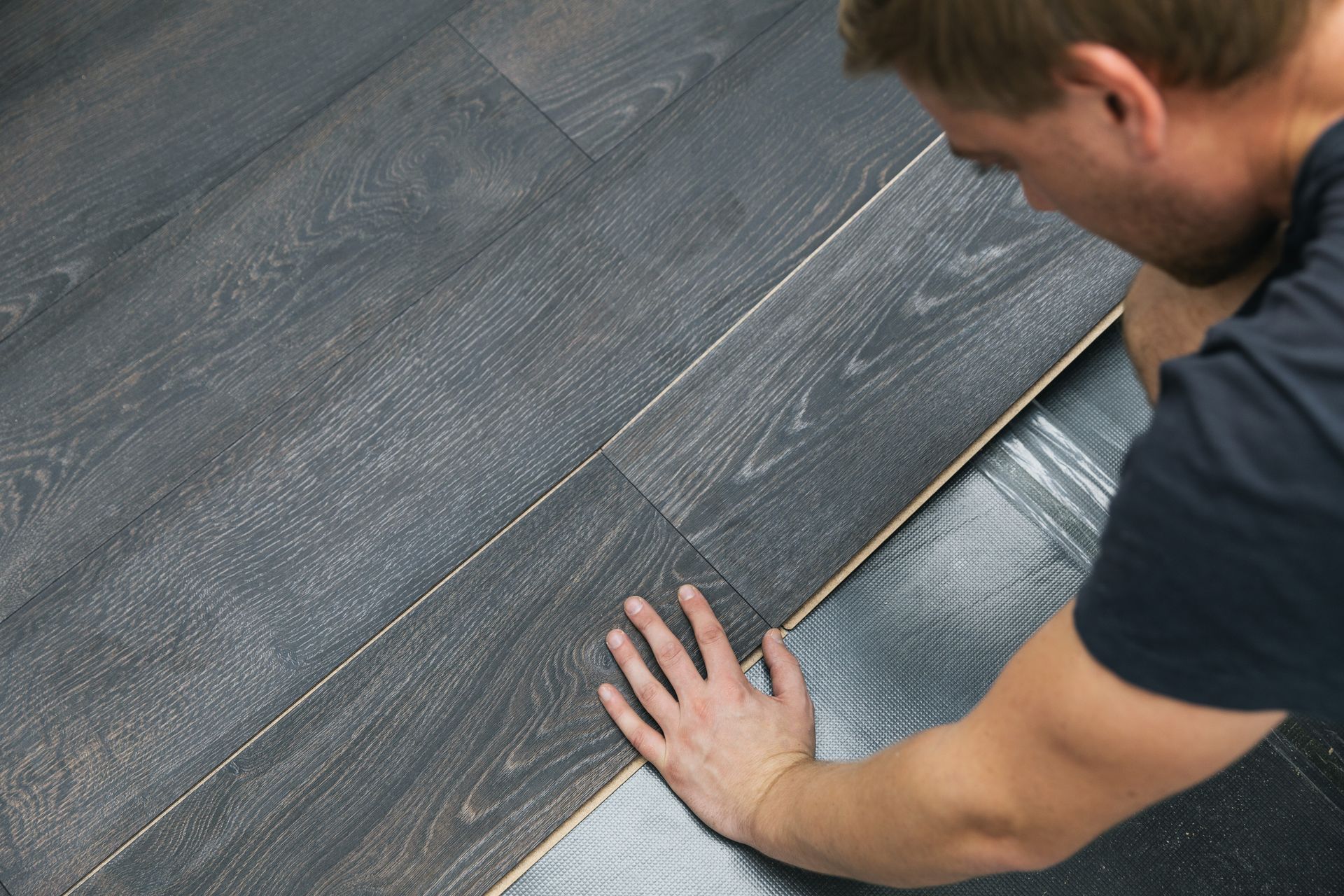 Person installing dark gray laminate flooring. Person installing dark gray laminate flooring.