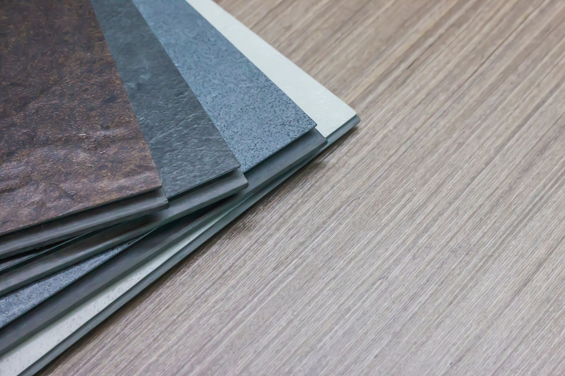Flooring samples: varying textures and colors displayed on a light wood surface. Flooring samples: varying textures and colors displayed on a light wood surface.