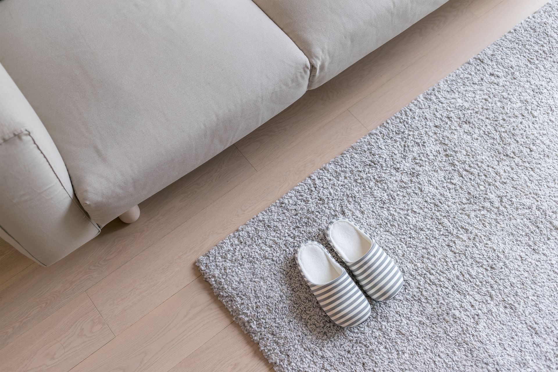 Beige sofa with grey rug and striped slippers on wooden floor. Beige sofa with grey rug and striped slippers on wooden floor.