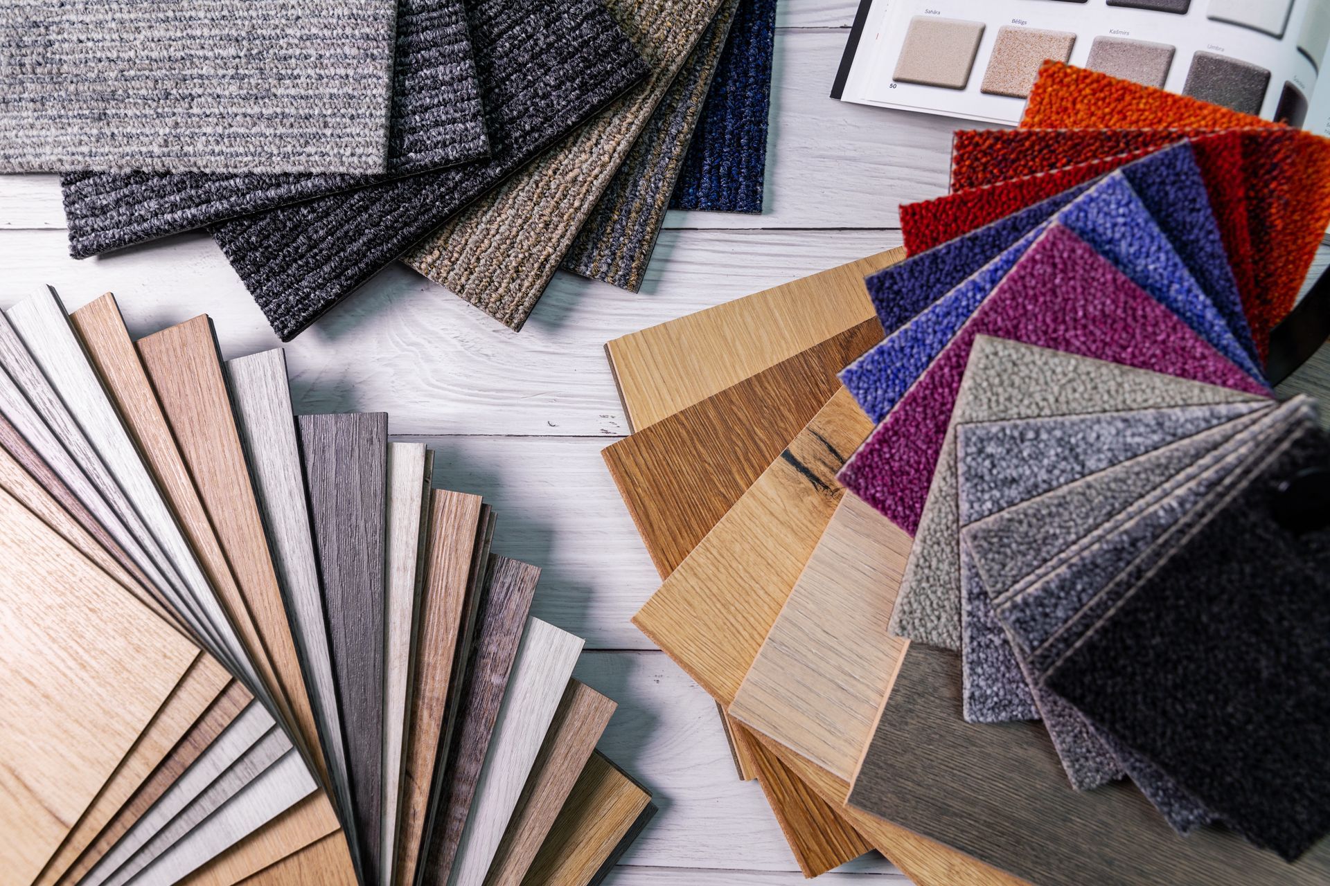 Assortment of flooring samples including wood, carpet, and textile swatches in various colors, arranged on a light wood surface. Assortment of flooring samples including wood, carpet, and textile swatches in various colors, arranged on a light wood surface.