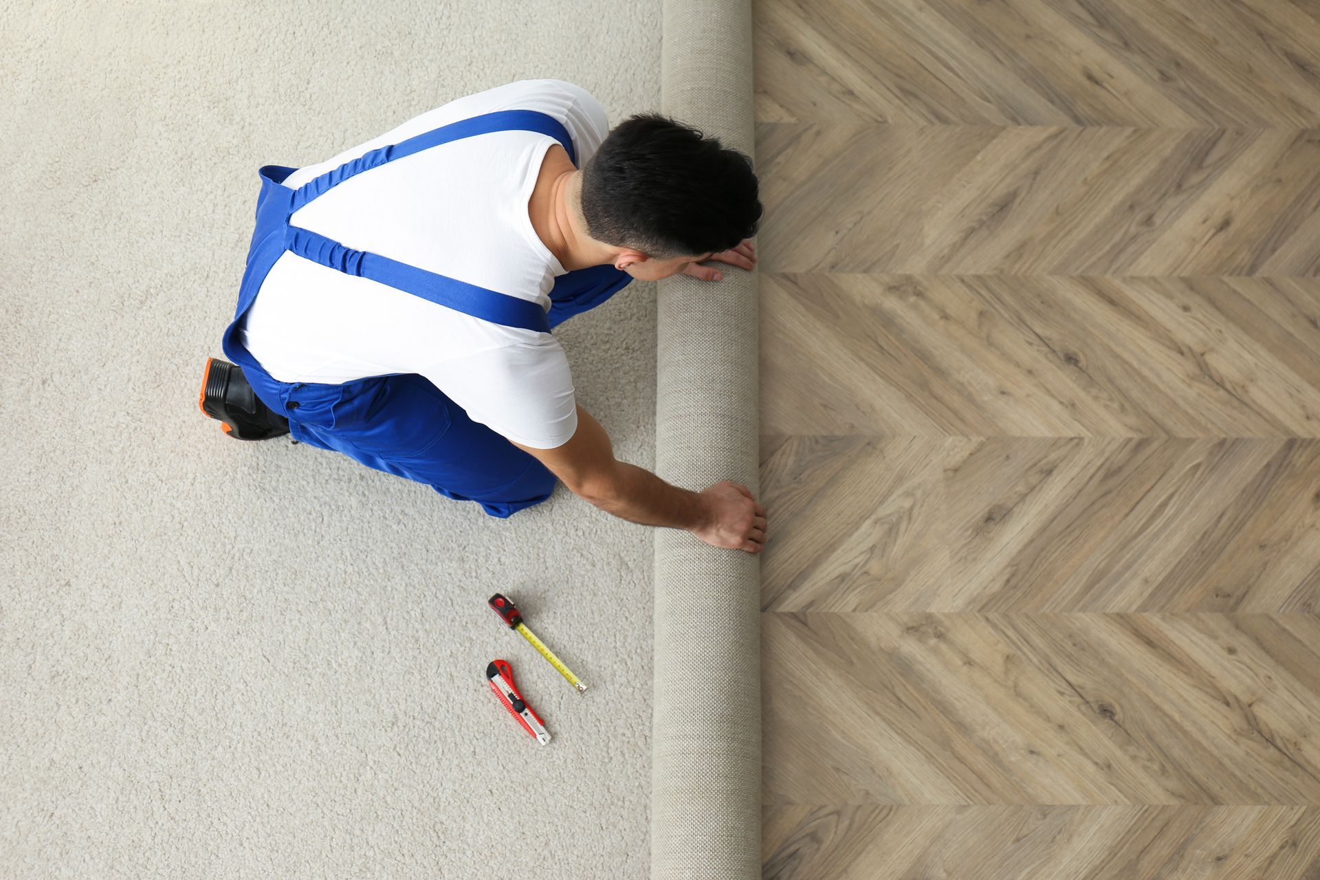A carpet installer is rolling back a carpet to fit hardwood flooring with tools nearby