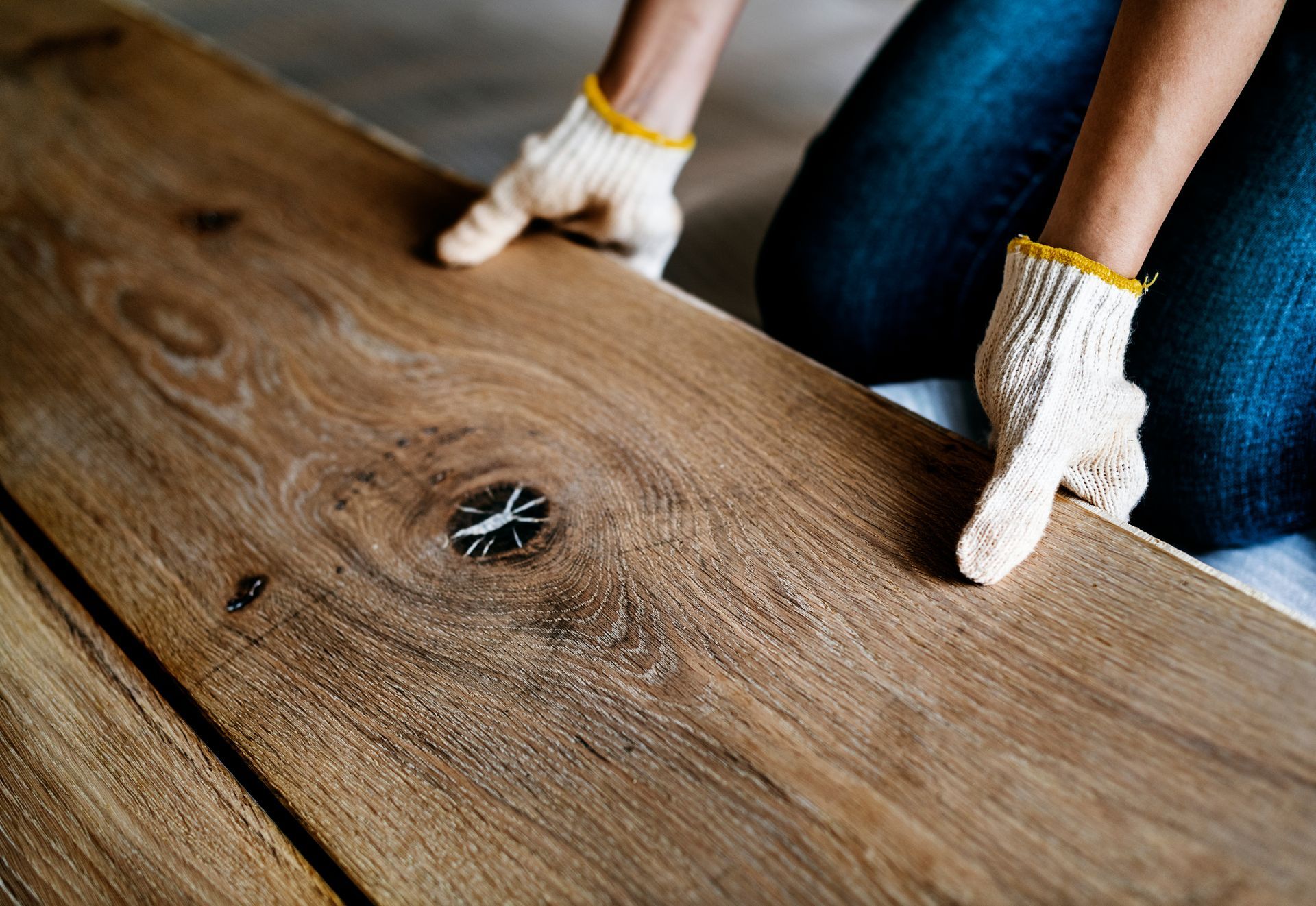Person wearing gloves installing wooden floor plank.