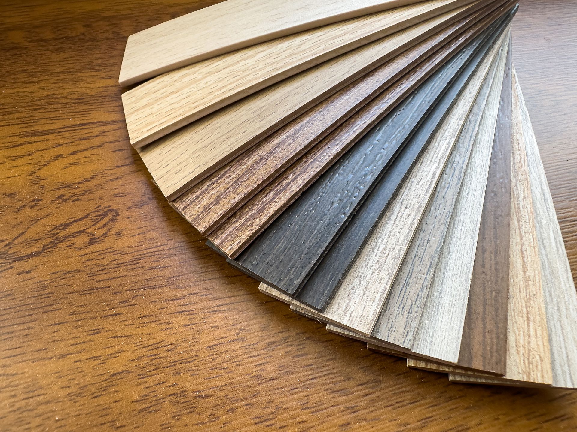Wooden flooring samples in various shades fanned out on a wood surface. Wooden flooring samples in various shades fanned out on a wood surface.