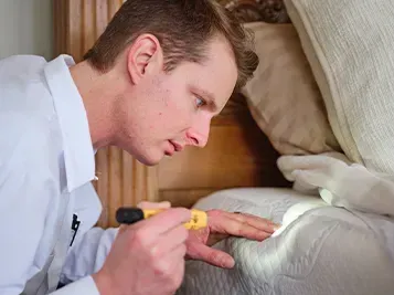 A man is looking at a bug on a bed with a flashlight.