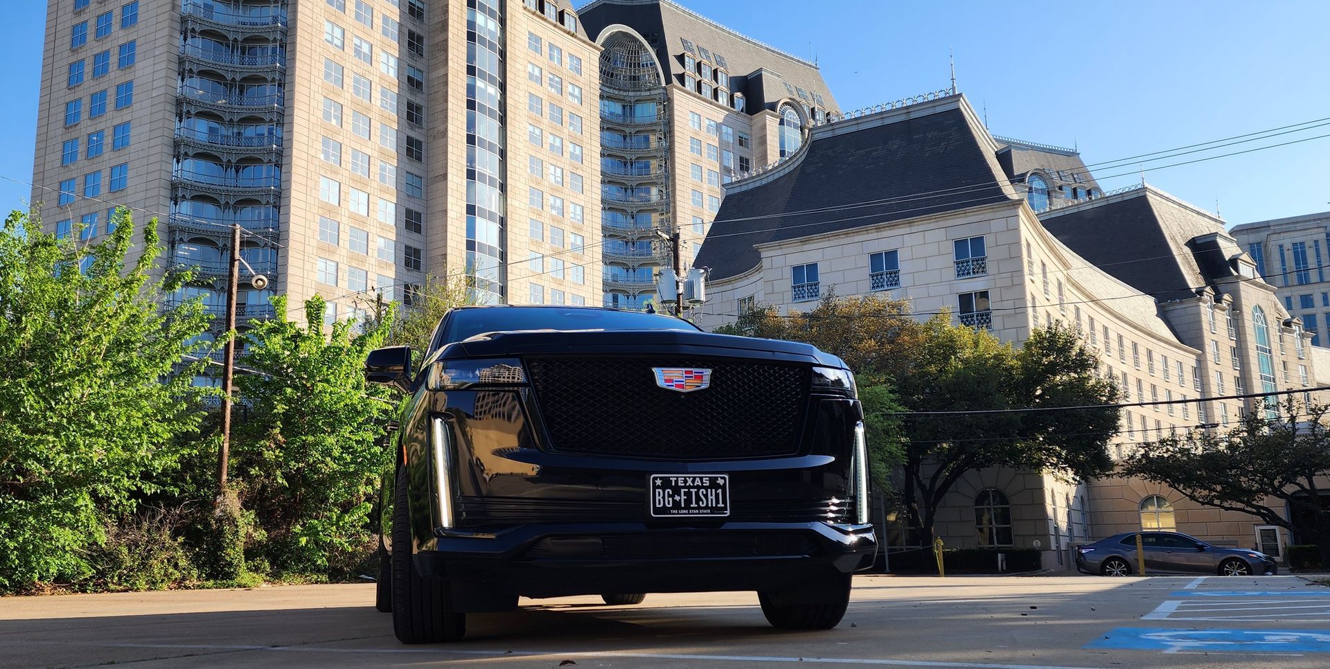 A black cadillac is parked in front of a tall building.