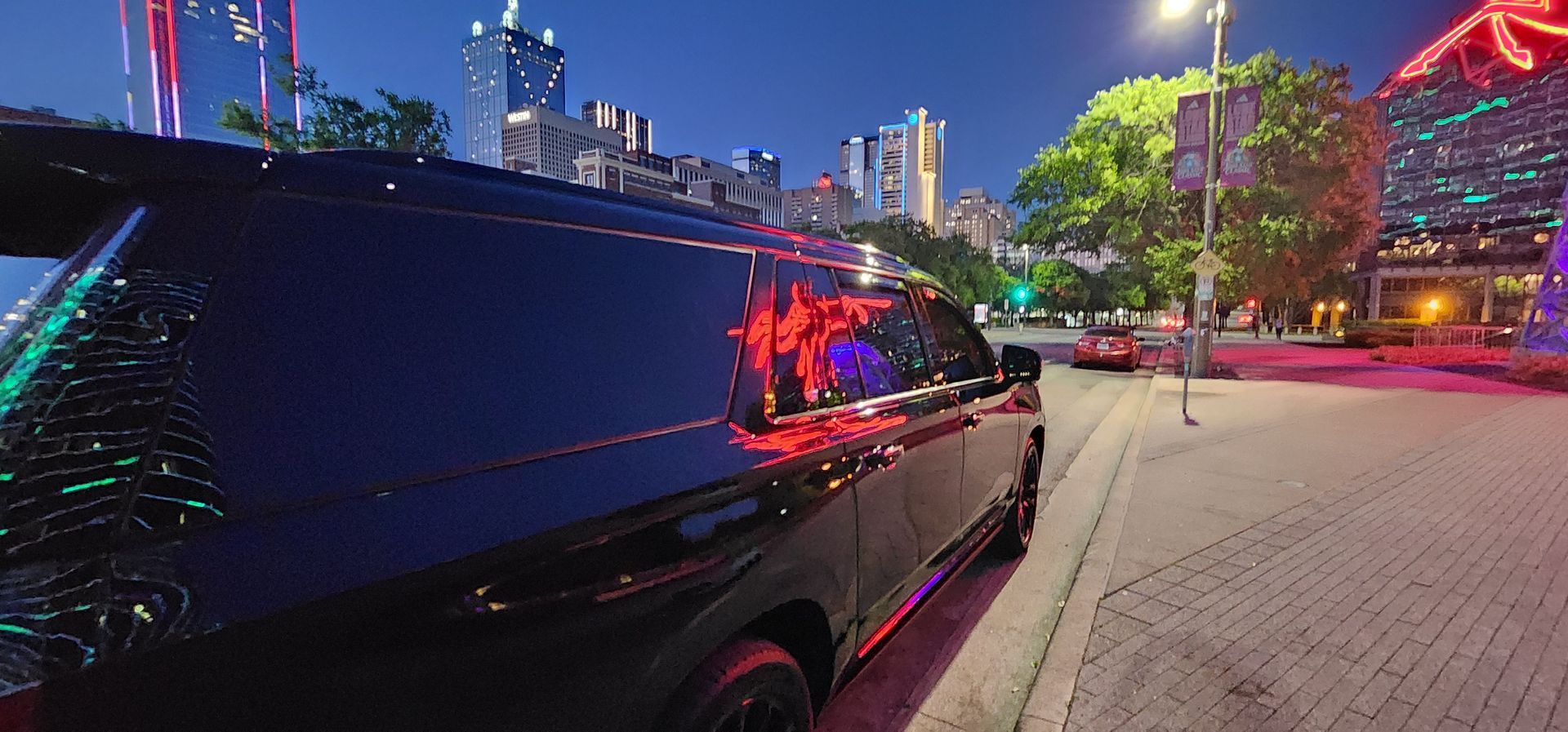 A black limousine is parked on the side of the road in front of a city at night.