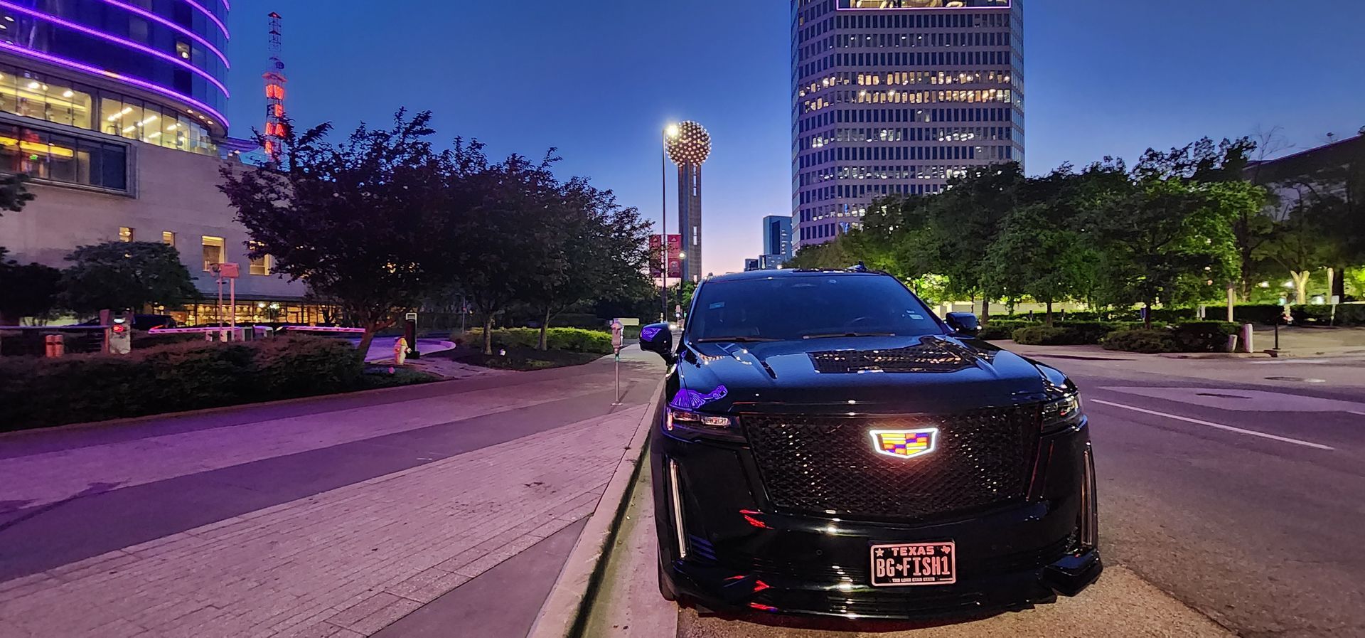 A black cadillac is parked on the side of a city street at night.