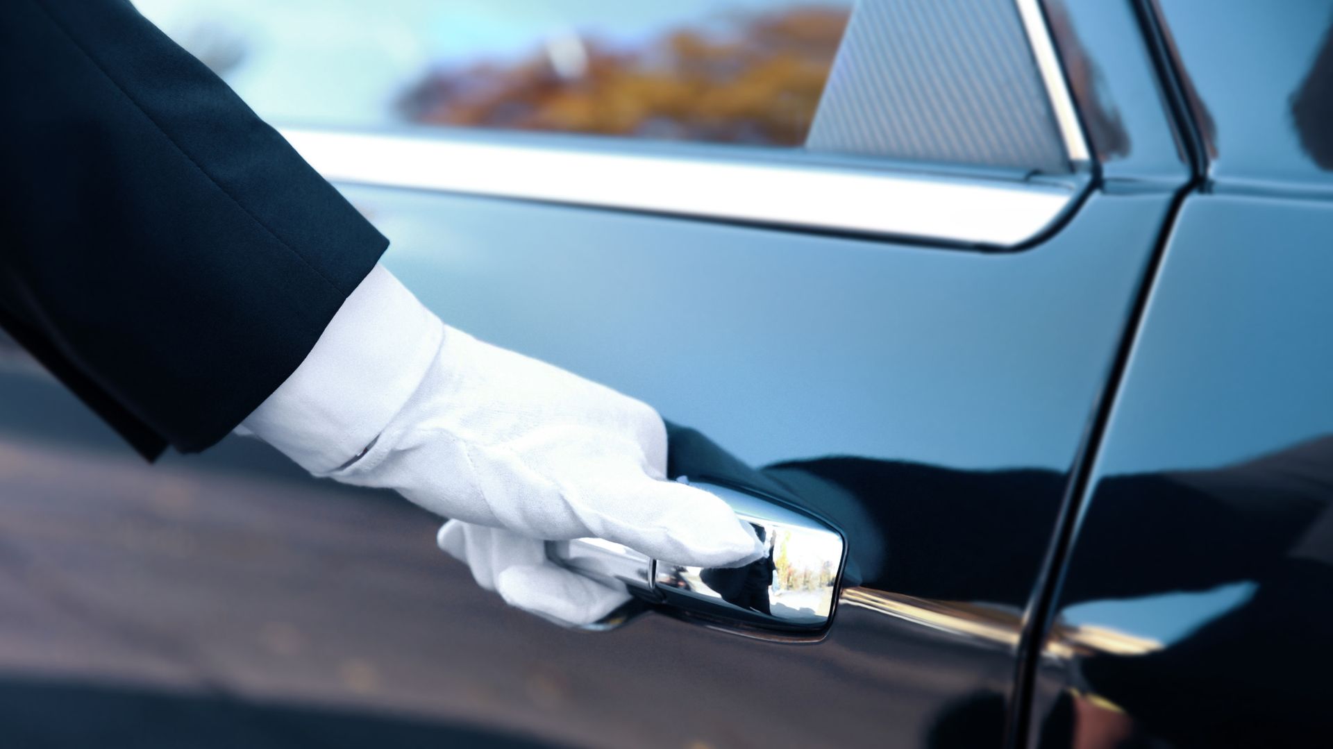 A person wearing white gloves is opening the door of a car.