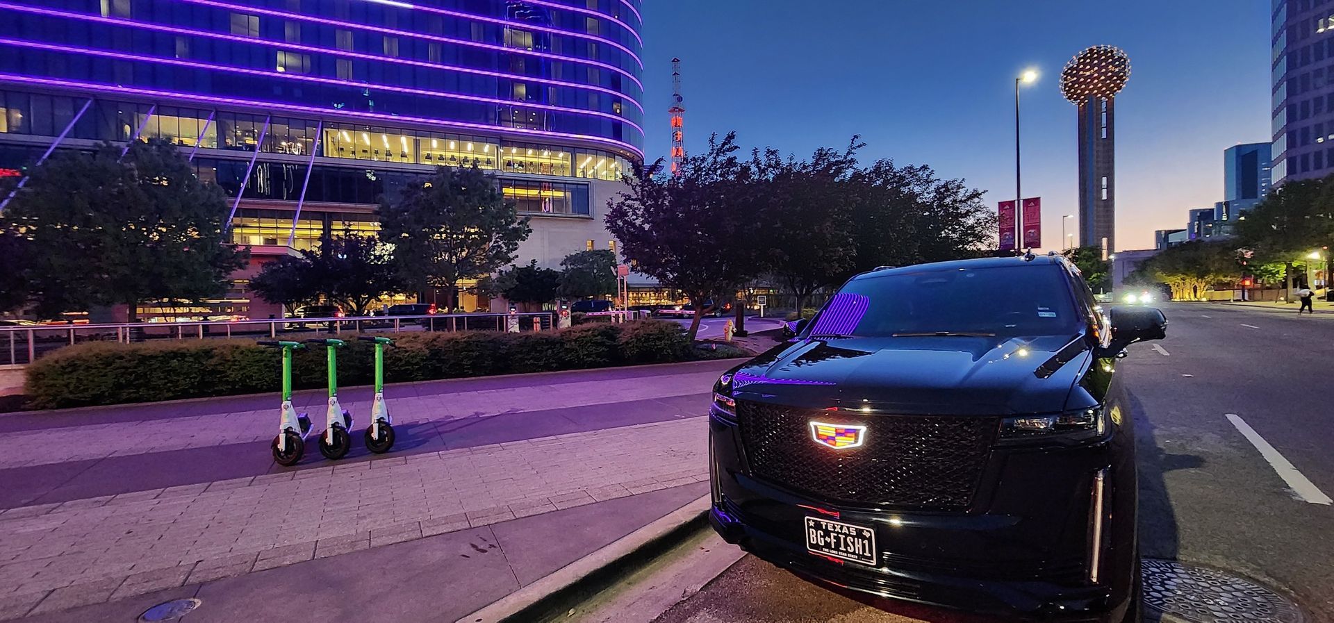 A black car is parked on the side of the road in front of a building with purple lights.