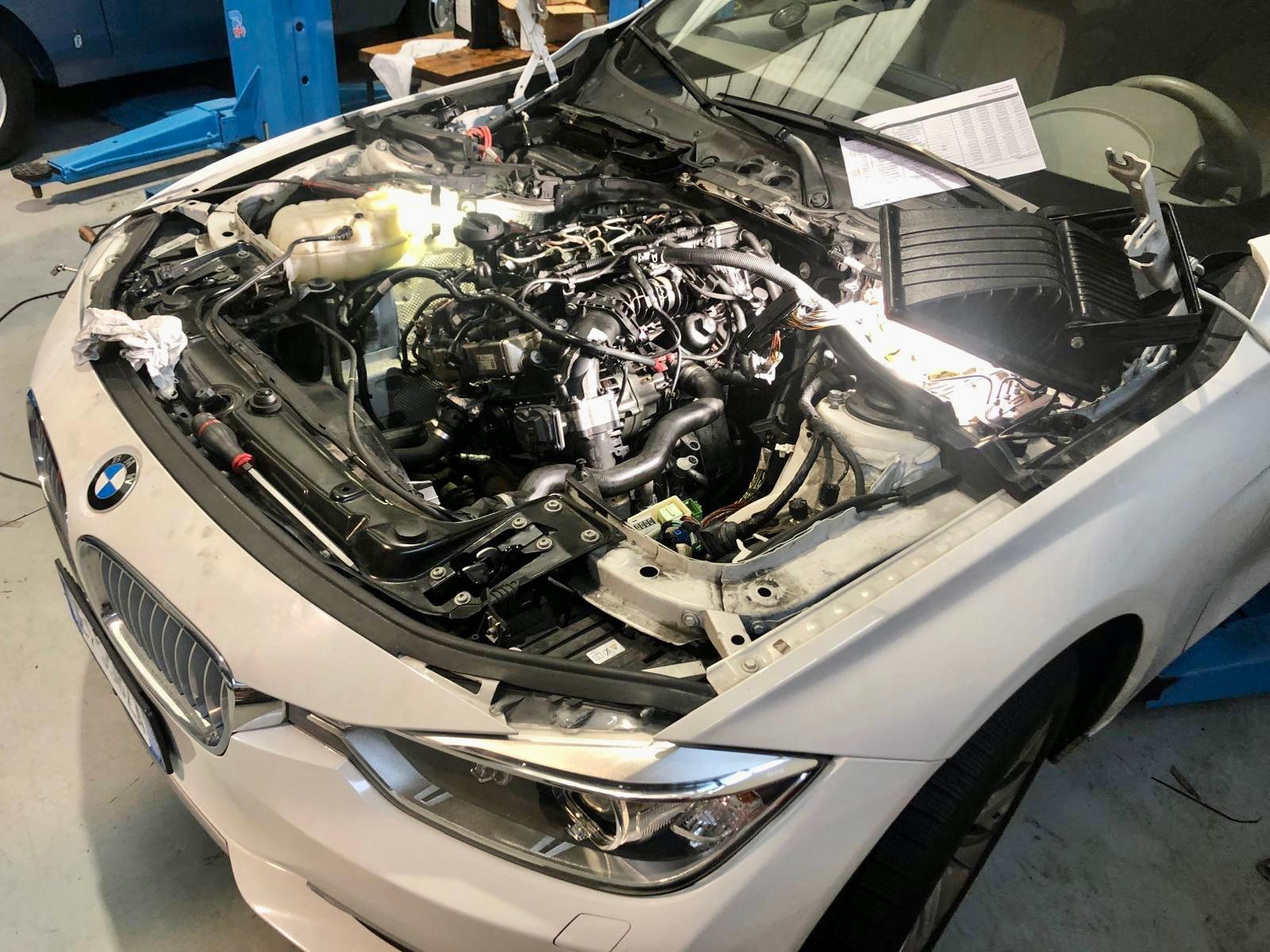 Una bmw bianca con il cofano aperto in un garage.