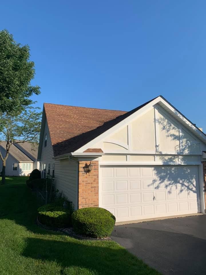 Beige house with a brown roof and white garage door against a blue sky.
