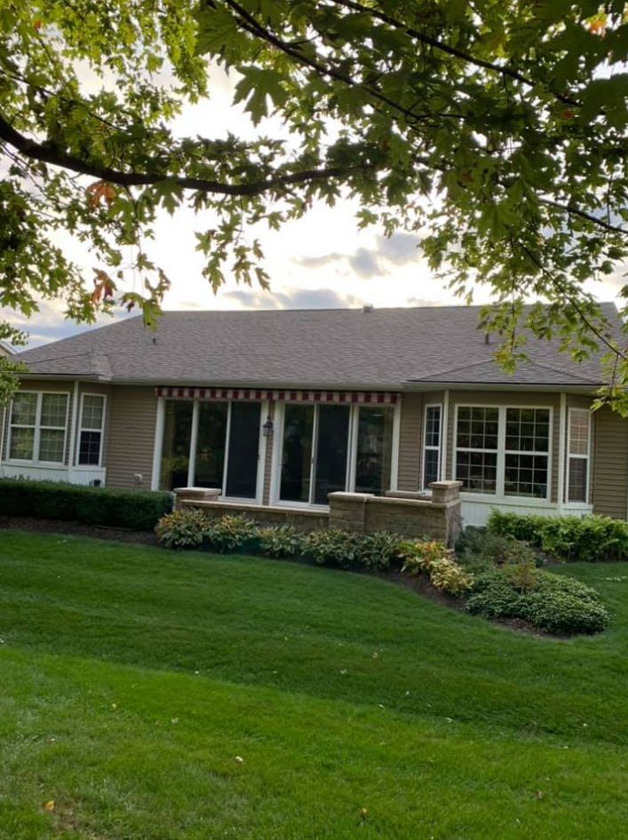 Beige house with a red and white awning, green lawn, and trees.